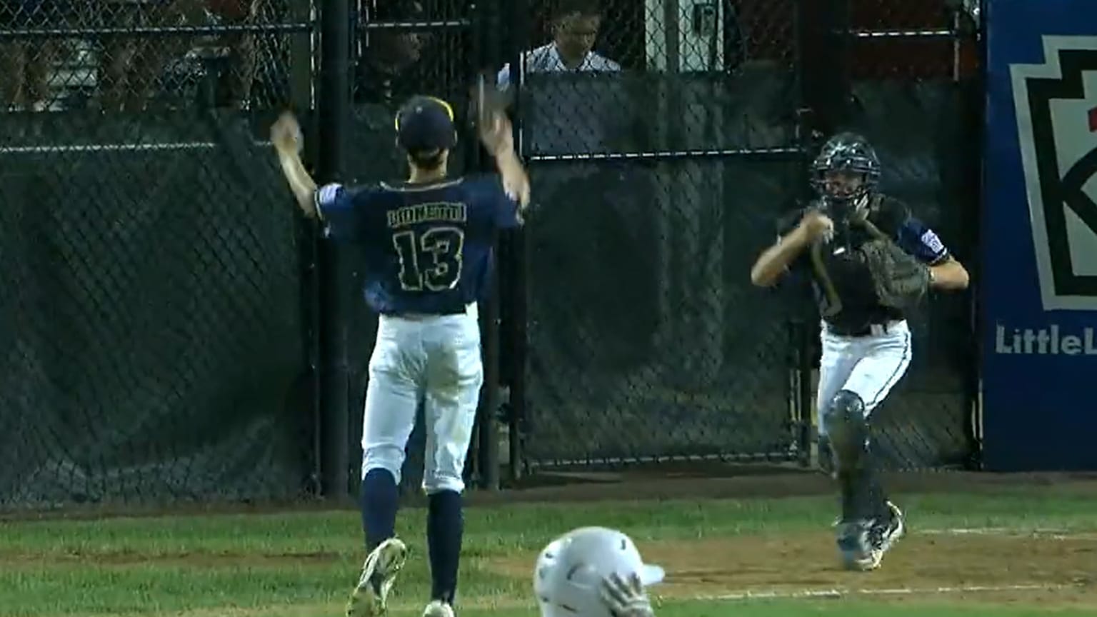 A Little League pitcher throws his arms in the air in celebration as the catcher runs toward him