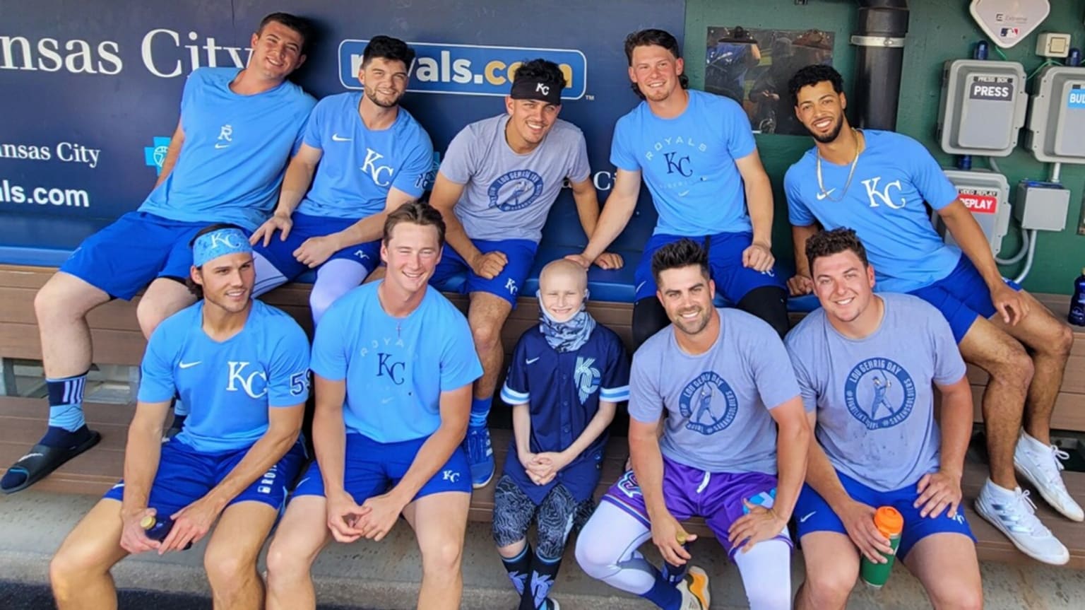Nine Royals players sit on the dugout bench around a young fan