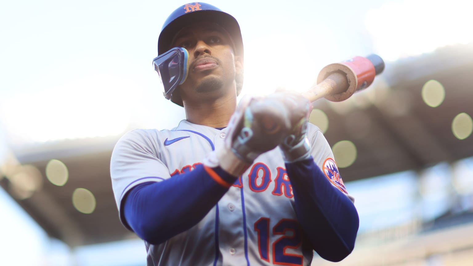 Francisco Lindor seen from a lower angle, holding a bat over his left shoulder. Sunlight behind him casts an ethereal glow