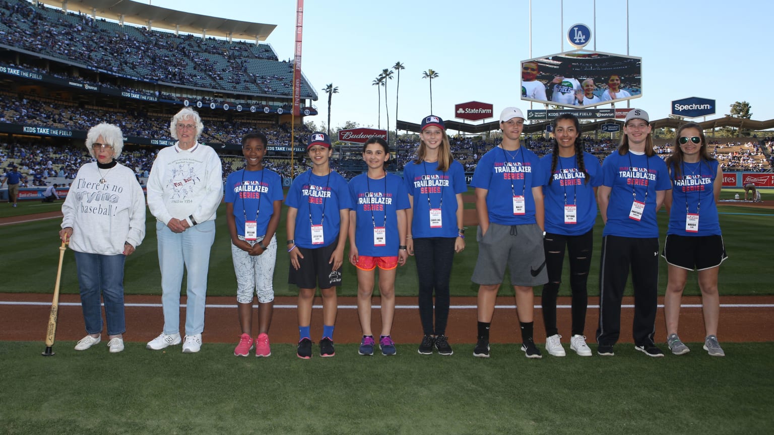 Two older women in white shirts stand with female youth ballplayers on a field