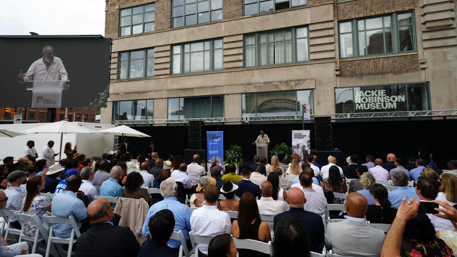 A seated crowd watches David Robinson speak on a street in front of the Jackie Robinson Museum in New York