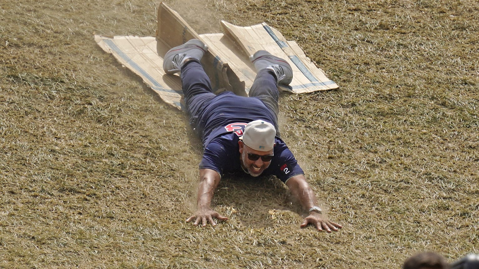 Red Sox manager Alex Cora slides off a piece of cardboard, continuing downhill on the grass