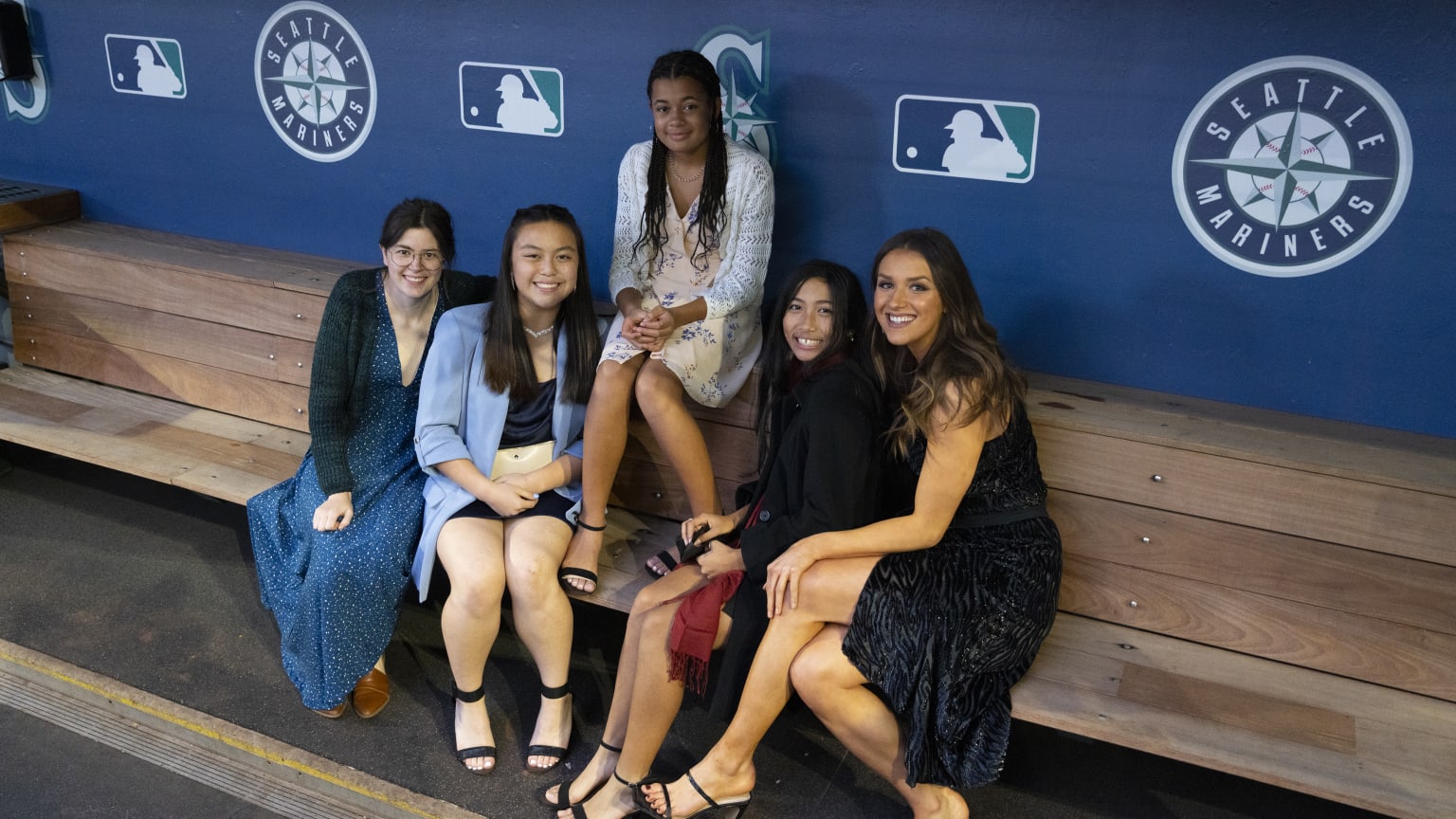 Group of women and girls sitting in a baseball dugout.