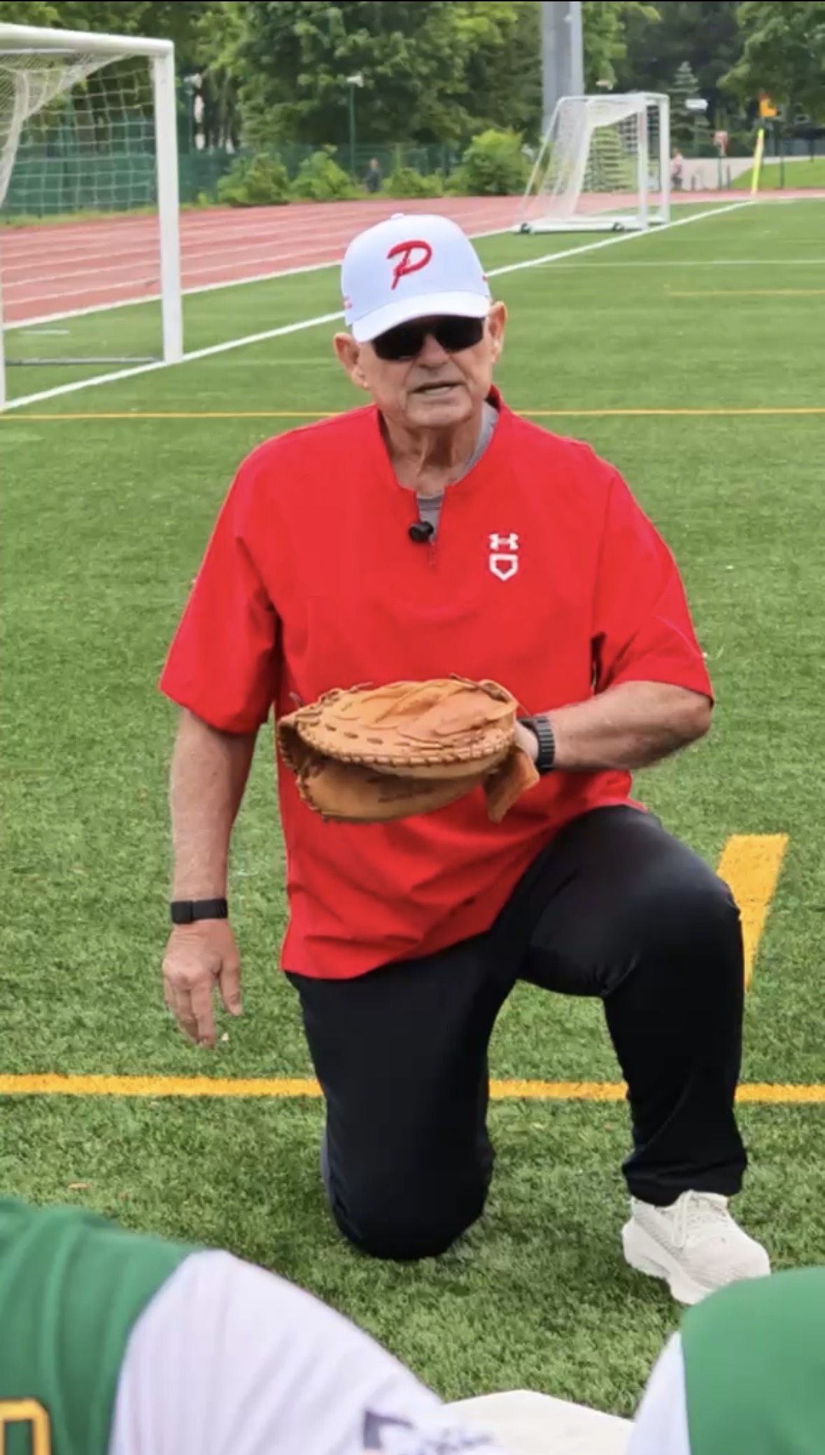 John McLaren takes a knee to give catching instruction to players in Poland. Photo by Markos Romo.