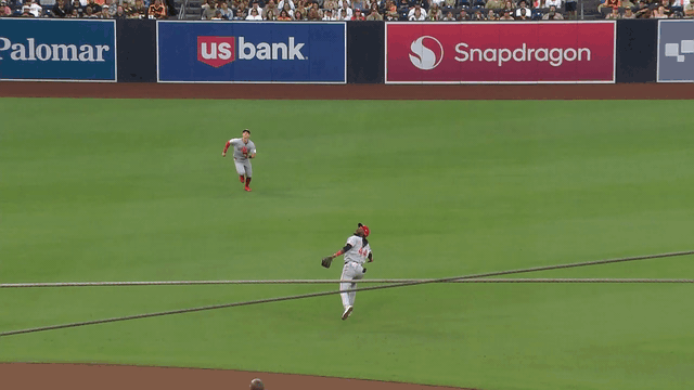 An animated gif of Elly De La Cruz making a backhanded, no-look catch over a sliding teammate
