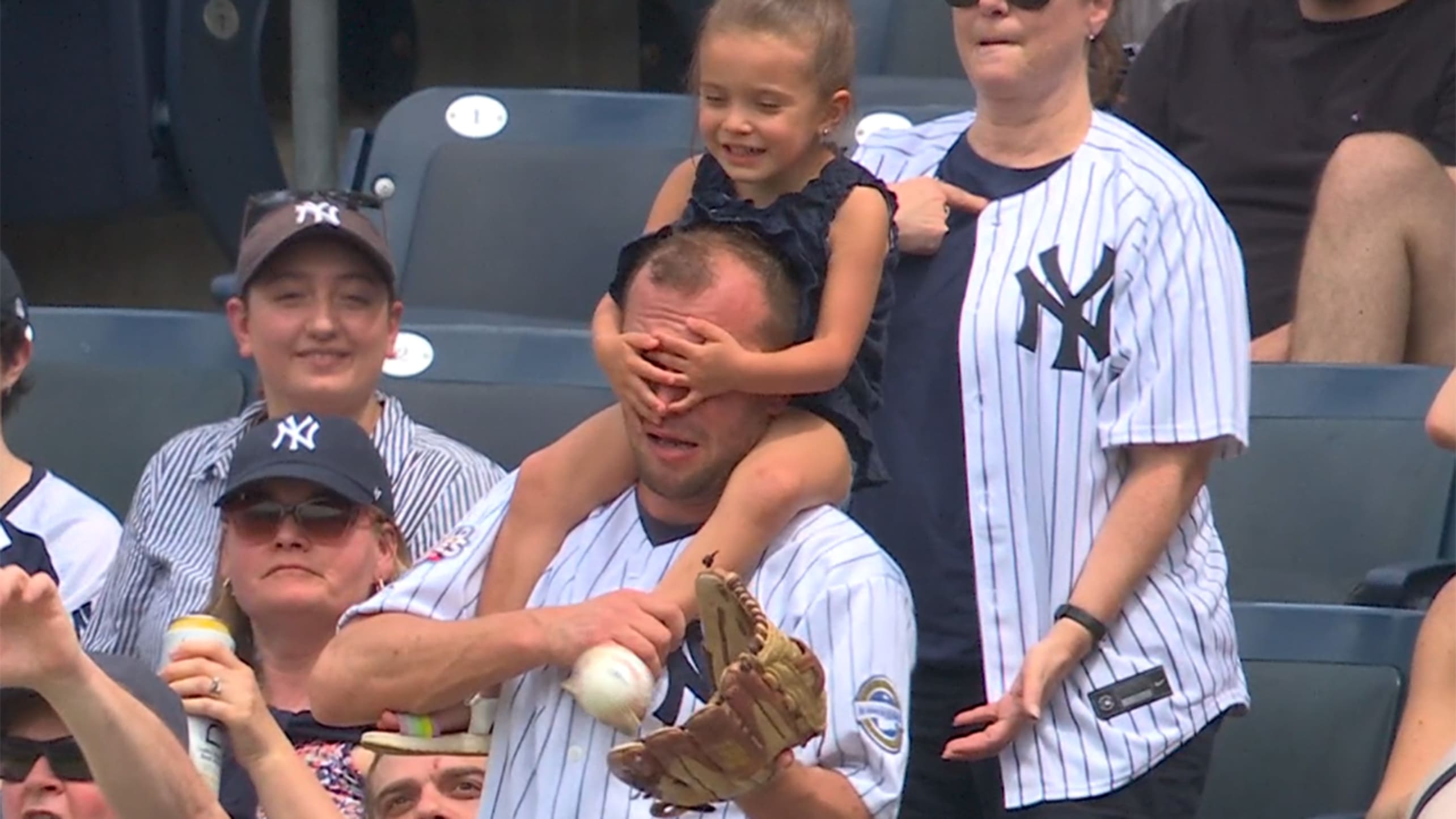 A fan reaches for a ball with his glove while a young girl covers his eyes with her hands