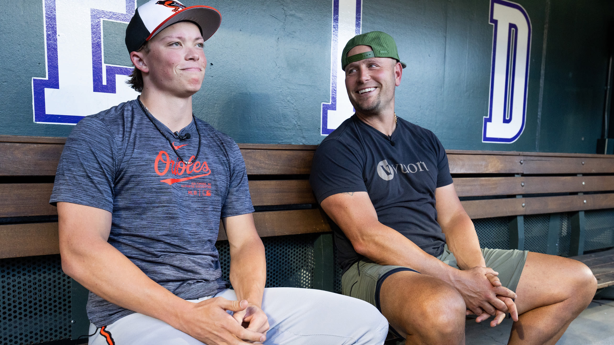 Jackson Holliday of the Orioles sits in the dugout at Coors Field with his dad, Matt, former Rockies star