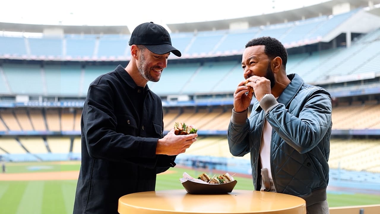 Mike Rosenthal and John Legend enjoy a bite standing at a table inside Dodger Stadium