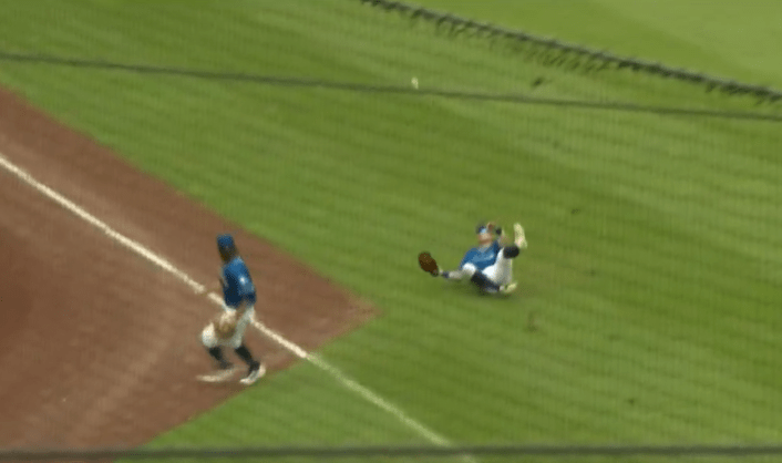 A ball is deflected by a left fielder as the third baseman looks on
