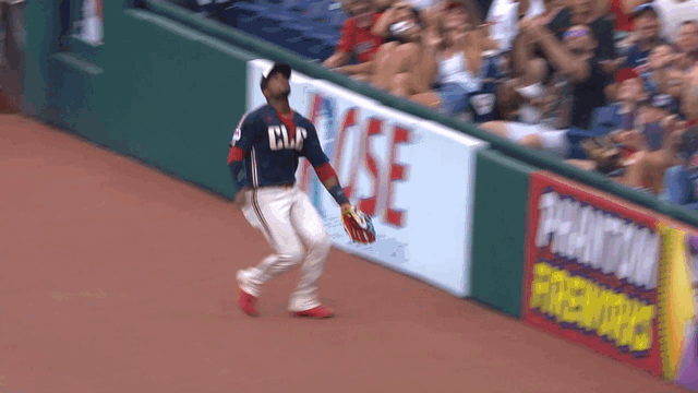 An animated gif of Angel Martínez making a leaping catch into netting in foul ground