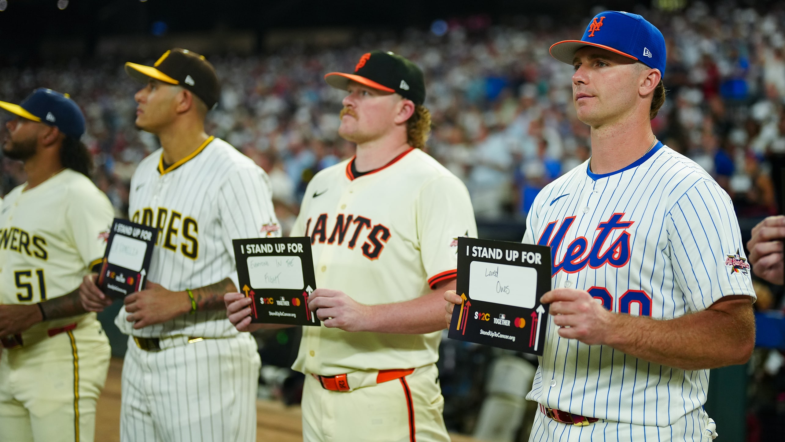 Freddy Peralta, Manny Machado, Logan Webb and Pete Alonso hold Stand Up 2 Cancer placards