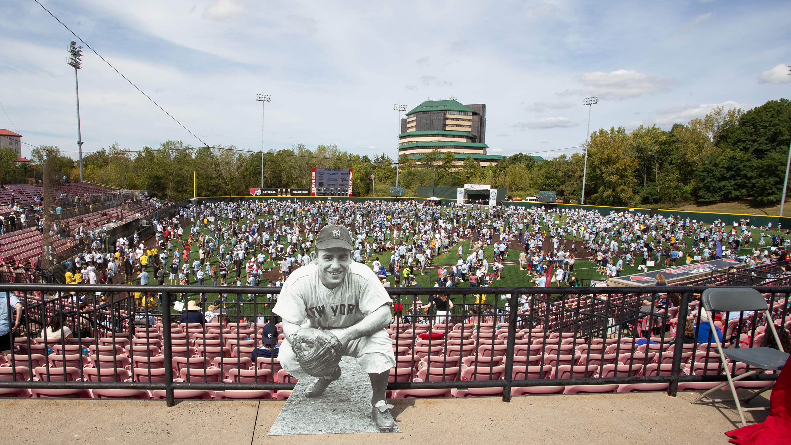 A cardboard cutout of Yogi Berra in front of thousands of people on a baseball field