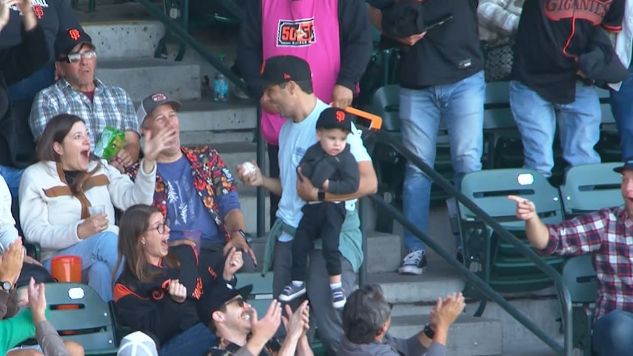 A fan holds a foul ball in one hand and his son in his other arm