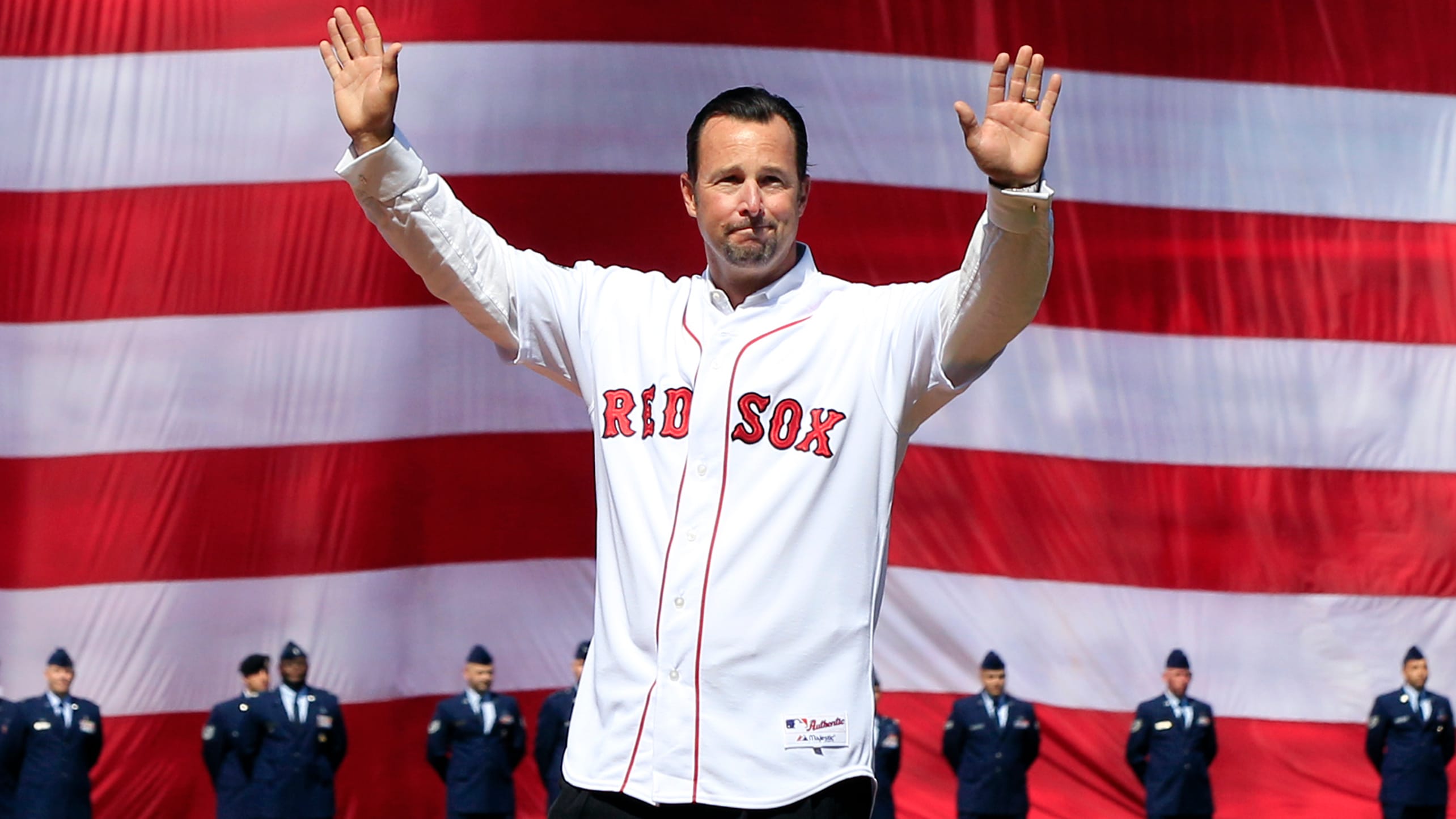 Wearing a Red Sox jersey and standing in front of a huge American flag, Tim Wakefield holds up both hands to wave to fans