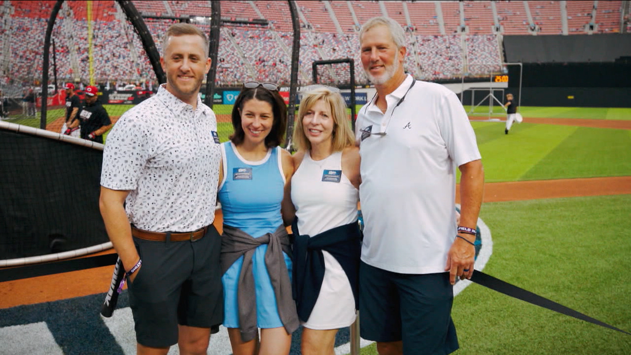 Four fans pose for a photo behind a batting cage