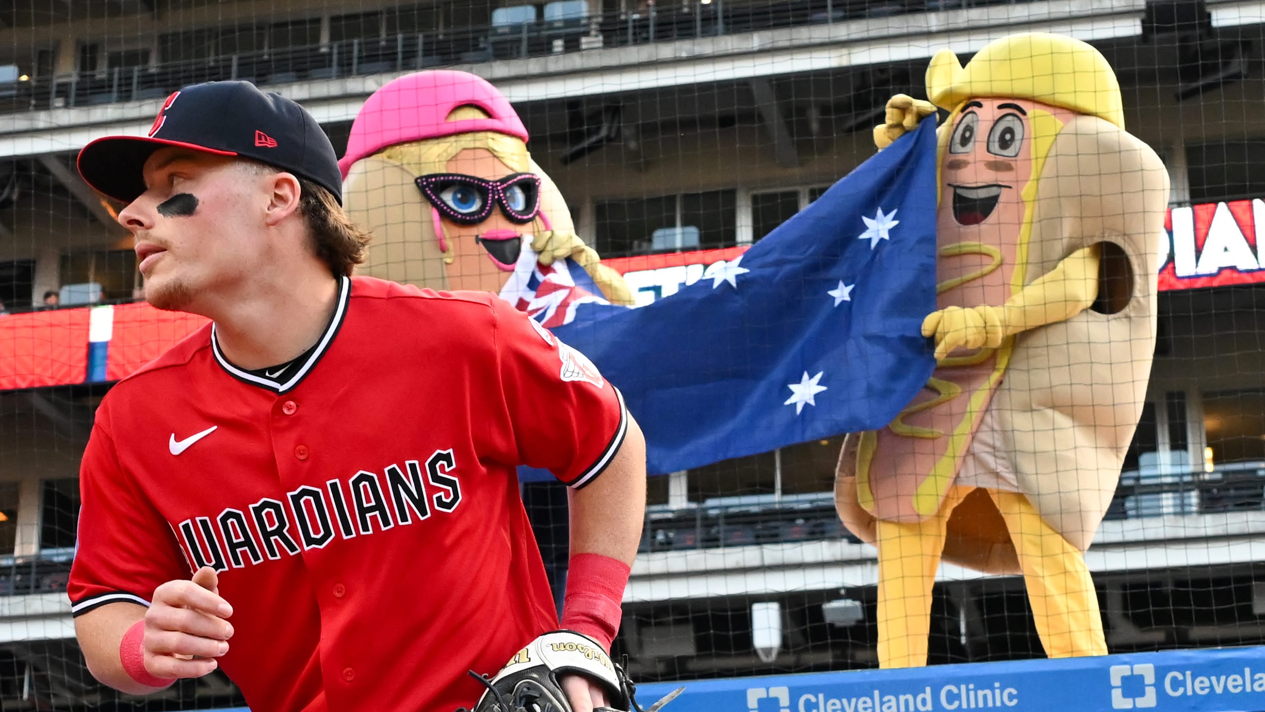 Travis Bazzana takes the field with two hot dog mascots holding an Australian flag behind him