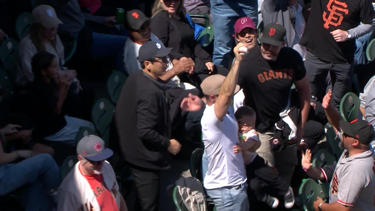 A fan holds up a foul ball he caught with a baby in his other arm