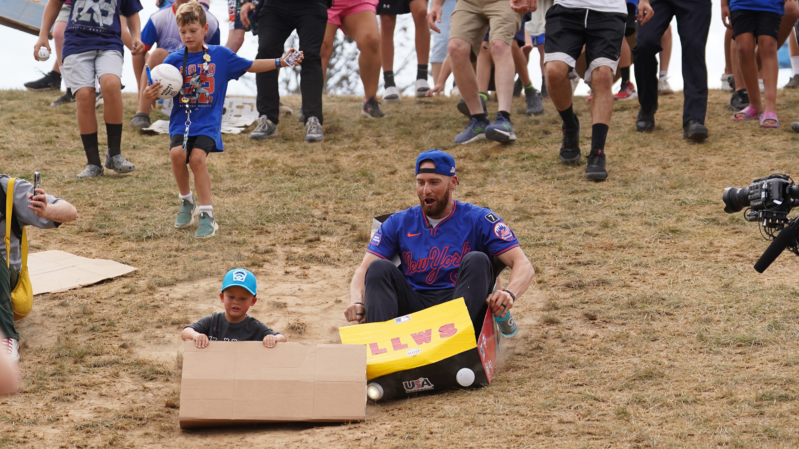 Brandon Nimmo and a child slide down a hill in cardboard boxes