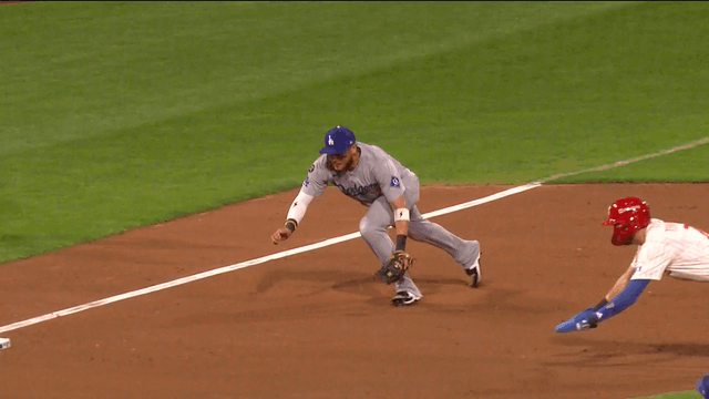 An animated gif of Dodgers third baseman Miguel Rojas diving to get the out at third base as the Phillies' Trea Turner slides in