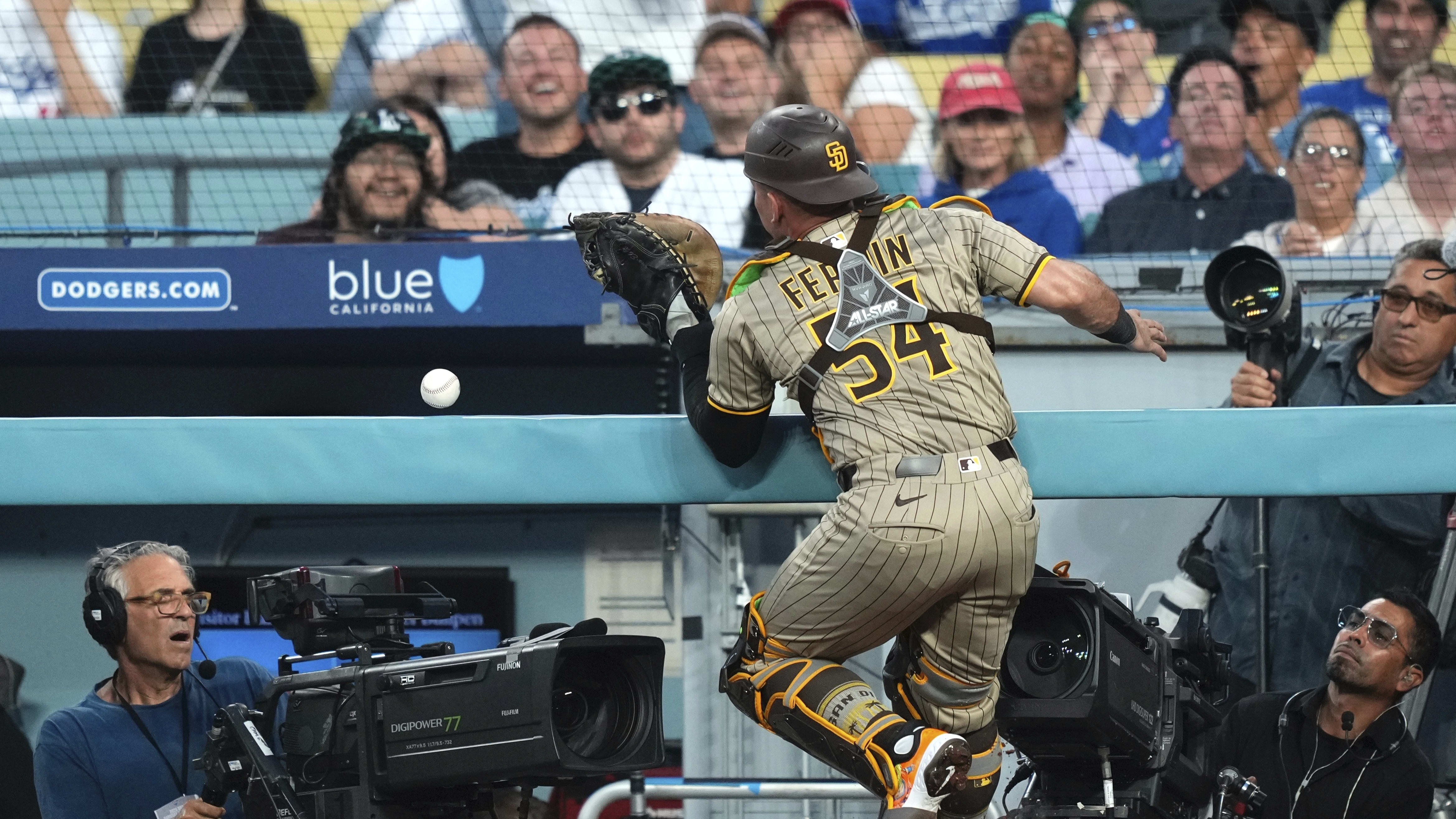 Padres catcher Freddy Fermin chases a foul ball into the railing above a cameraman