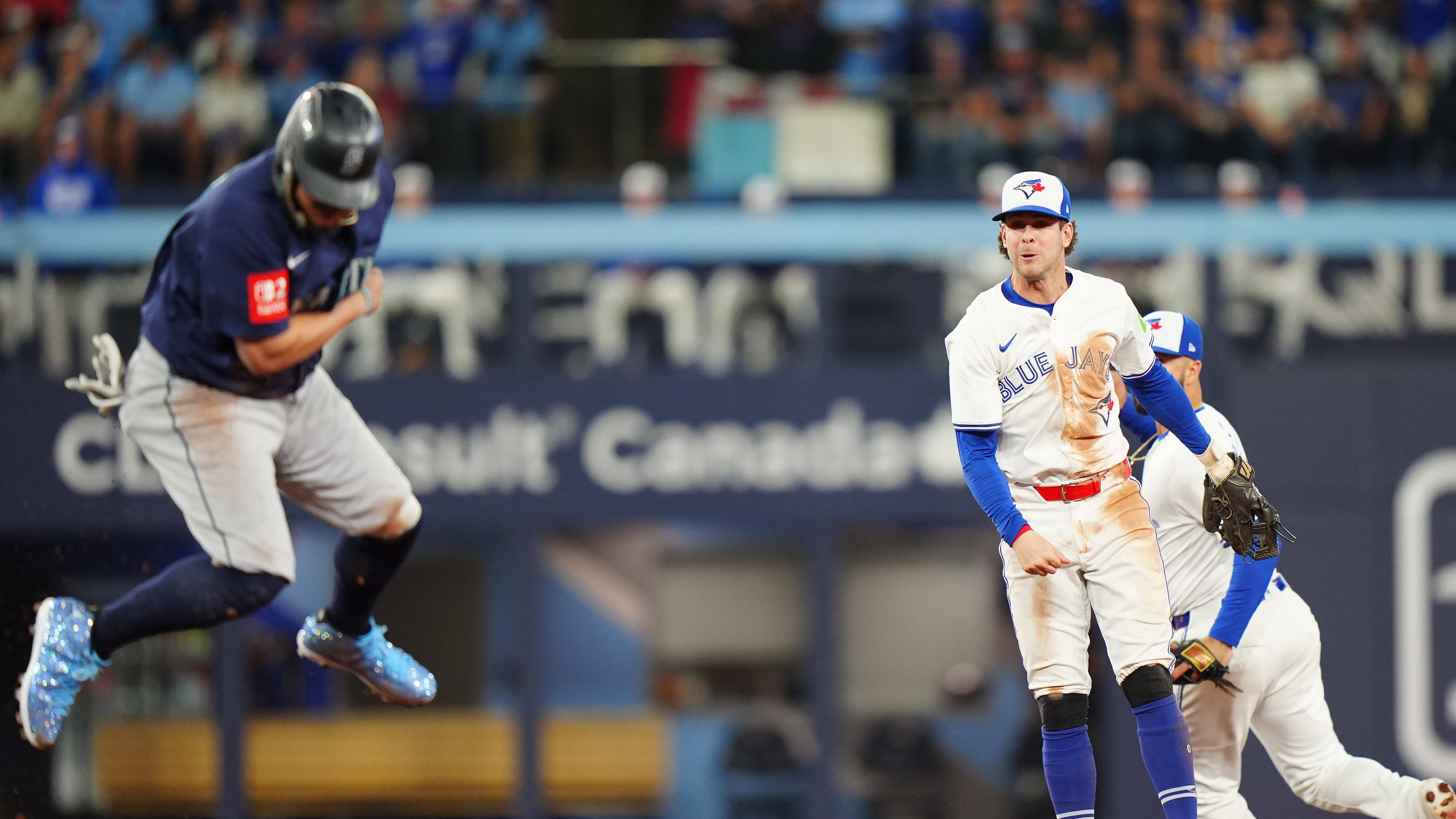 Josh Naylor leaps on the basepaths as Blue Jays third baseman Ernie Clement watches