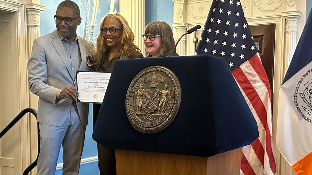 Yankees SVP of corporate/community relations Brian Smith and Food Bank for NYC's Janis Robinson receive the award from NYC chief service officer Laura Rog.