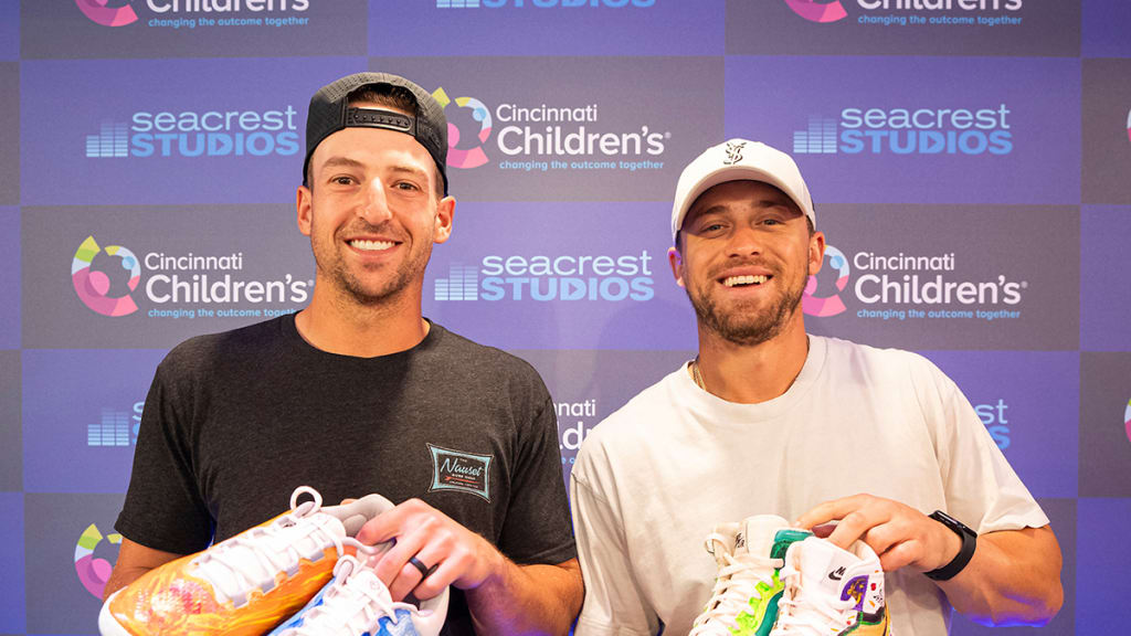 Reds players Spencer Steer and TJ Friedl hold custom cleats painted by kids at Cincinnati Children's Hospital for Players' Weekend.