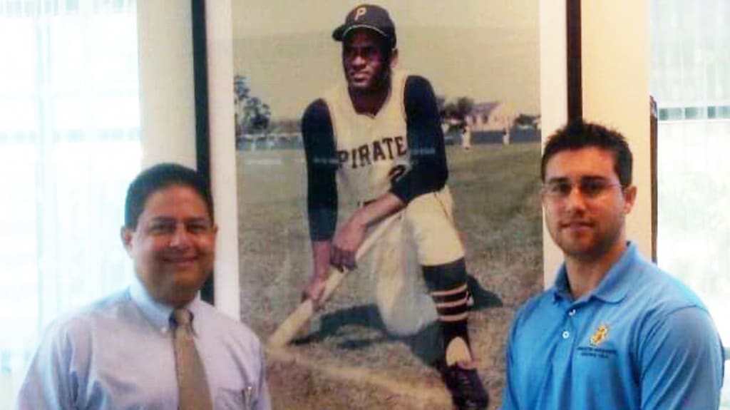 Juan Rodríguez with his father in front of a Roberto Clemente photo while working with the Pirates.