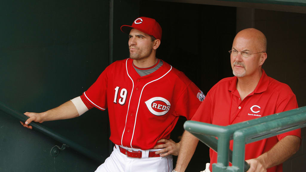 Joey Votto (left) and longtime team doctor Timothy Kremchek look on from the dugout.