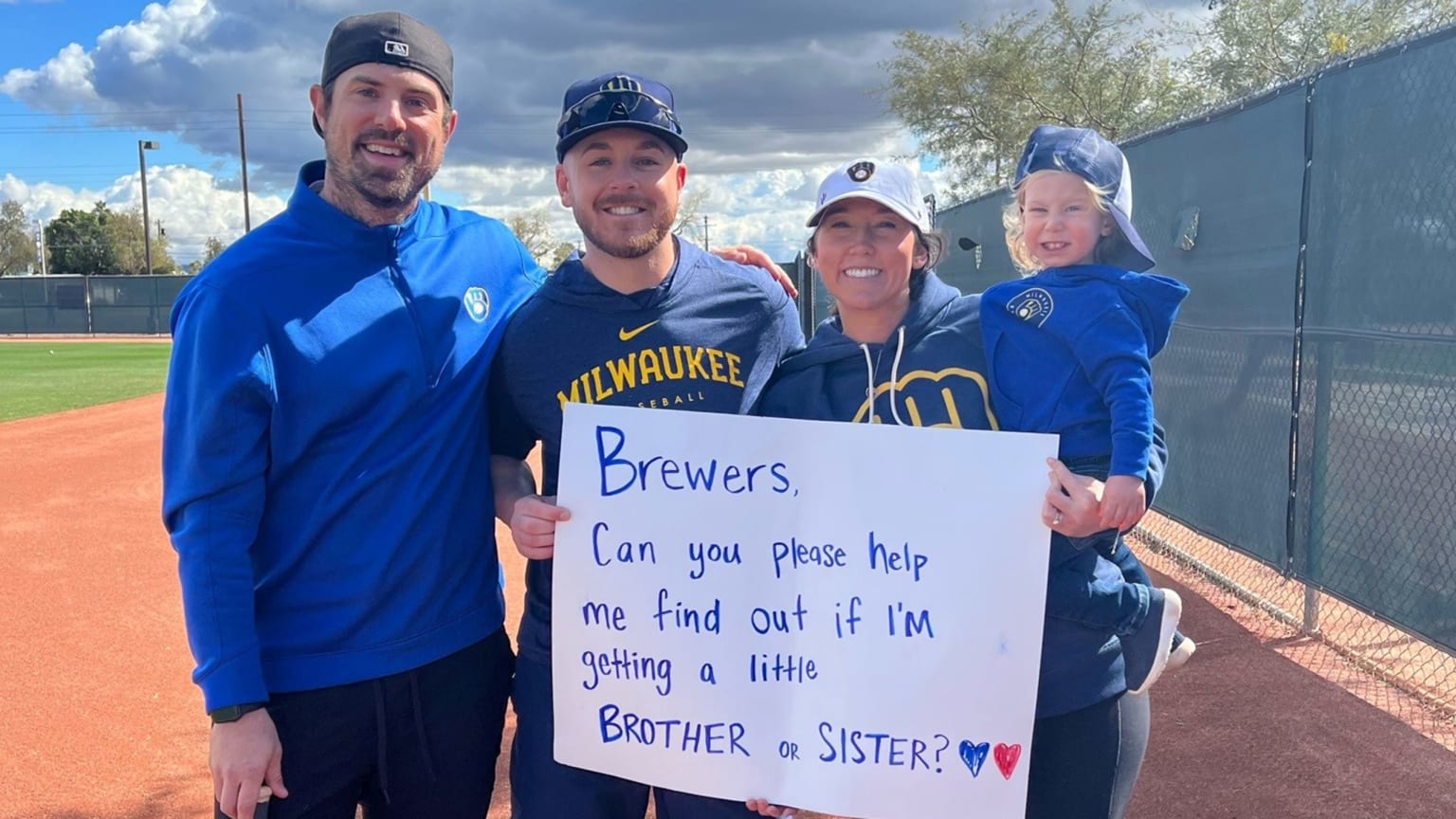 A Brewers player stands with a couple and their baby, two of them holding a sign