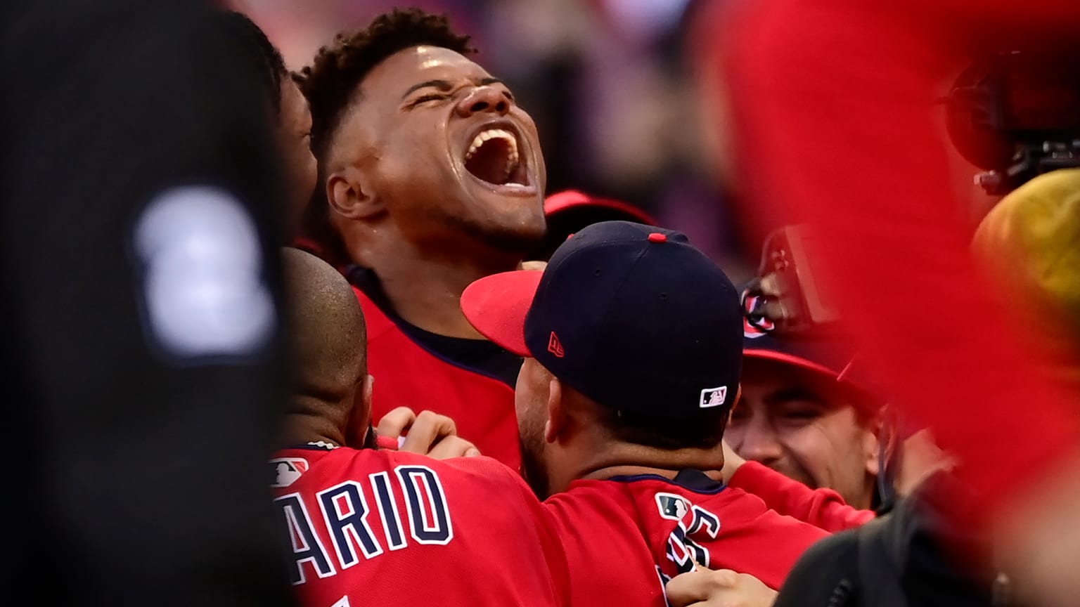 A man leans his head back and screams in celebration while surrounded by players in red jerseys