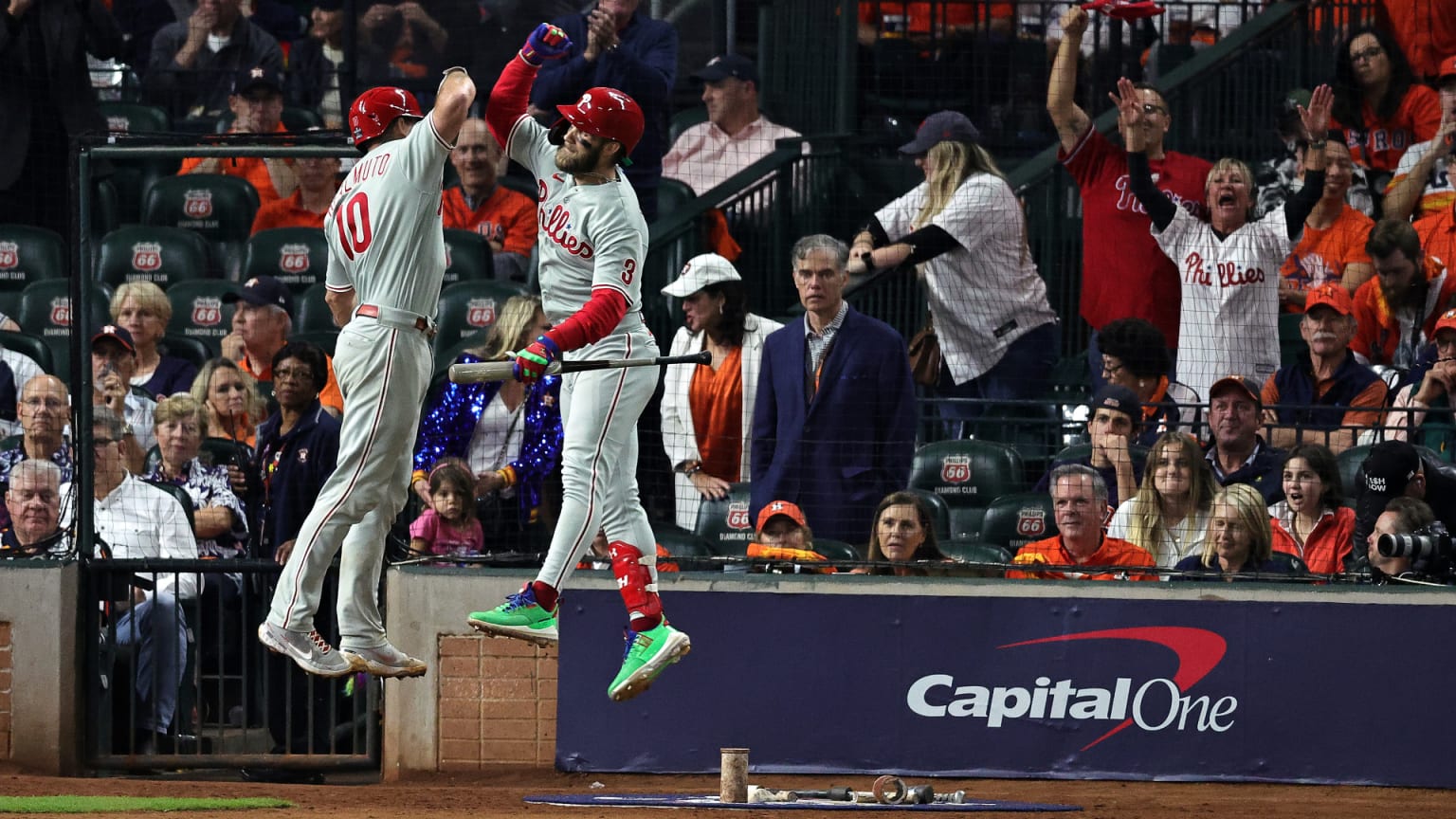 Two Phillies leap in the air to high-five near the stands