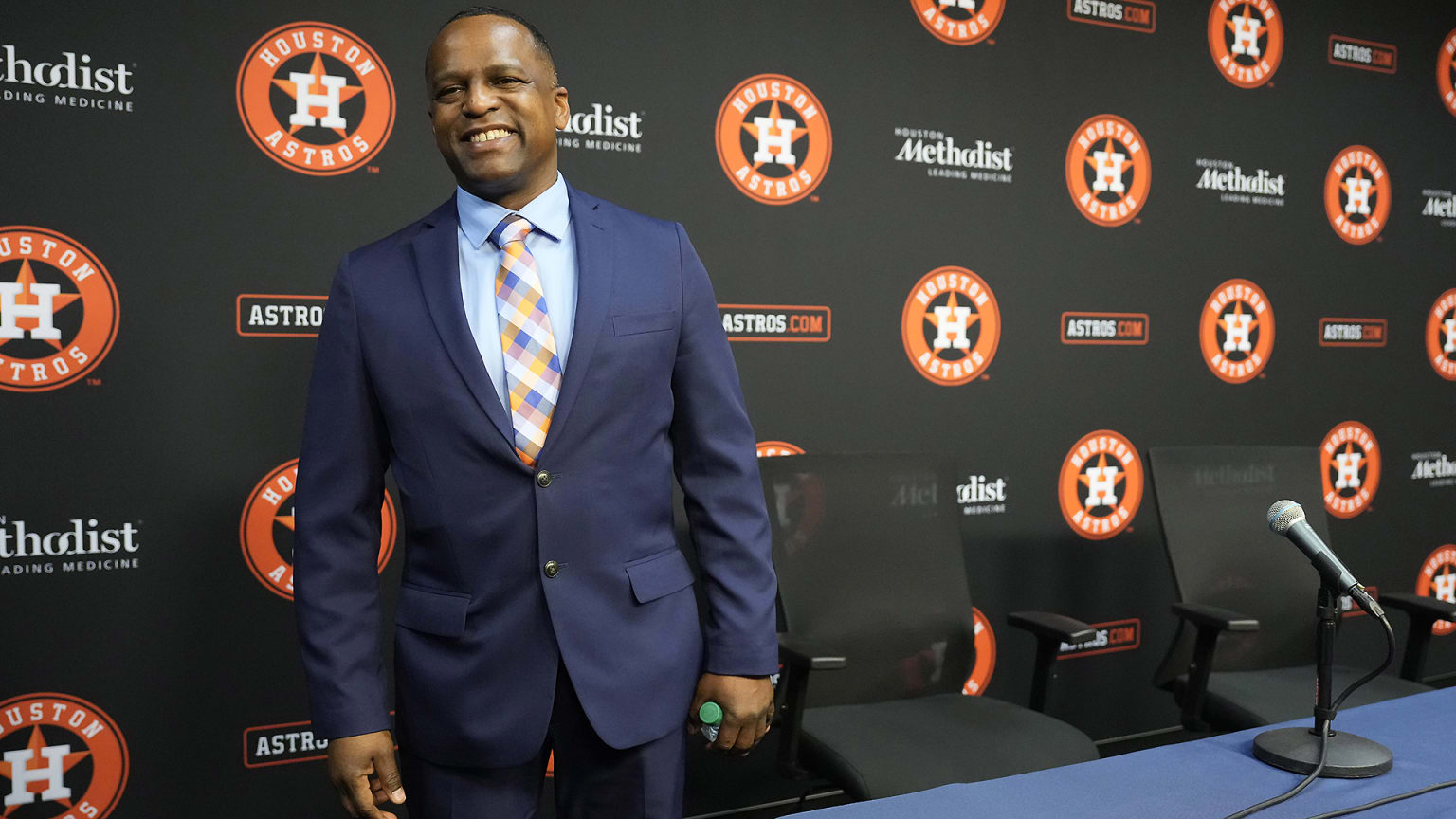 Astros GM Dana Brown in a suit behind a table with a microphone on it