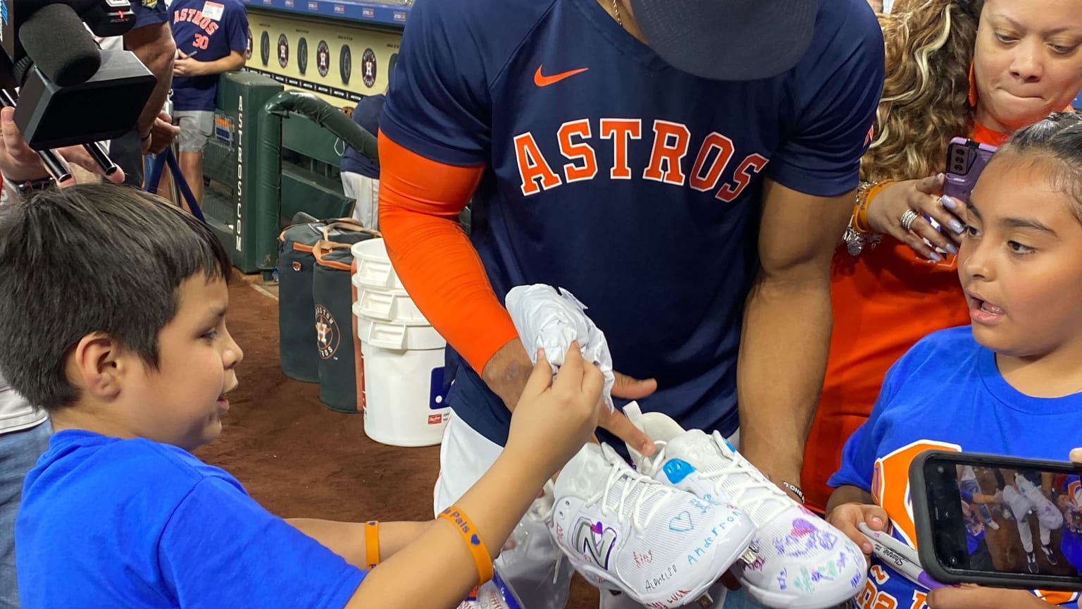 Jeremy Peña looks at a pair of white cleats with two young fans on either side of him