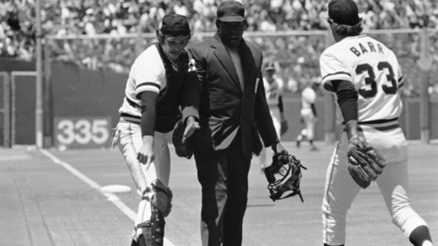 A black-and-white photo of a catcher pointing to the ground next to a Black umpire in a black suit