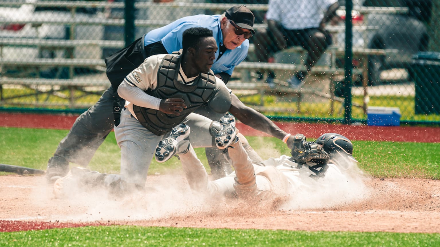 A catcher tags a runner sliding home in a cloud of dust as an umpire leans in for a good look