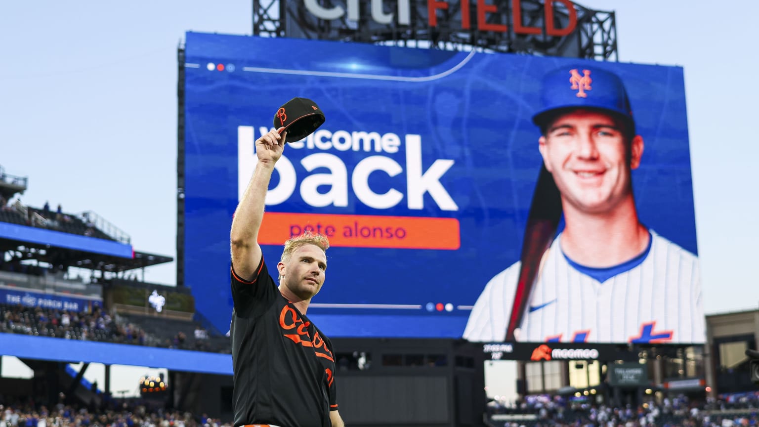 Pete Alonso waves his cap to the fans at Citi Field, with a 'Welcome Back' greeting on the video board behind him