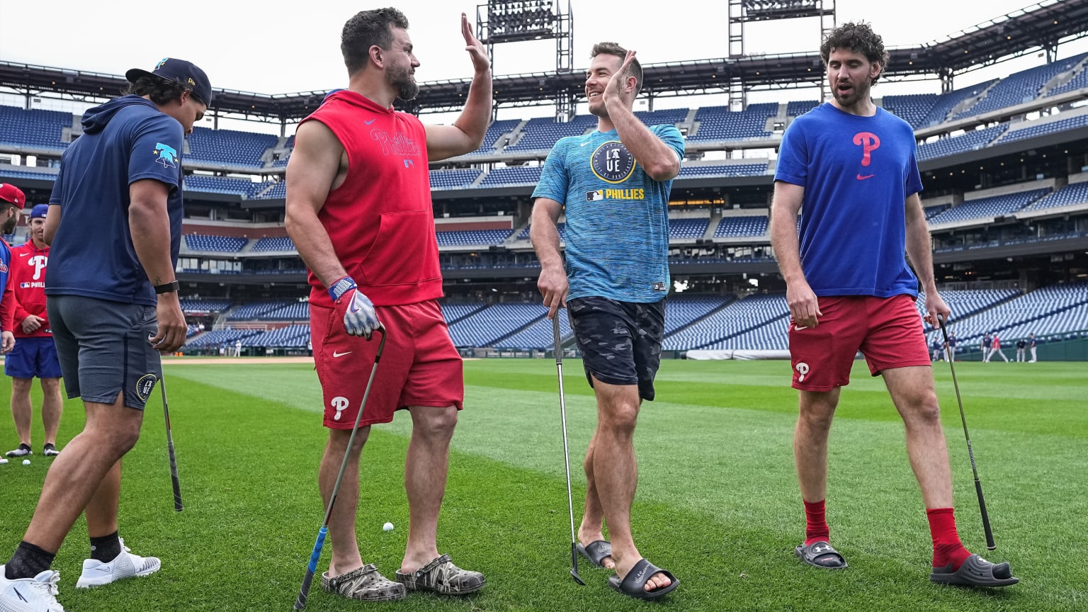 Four Phillies players hold golf clubs and two of them high-five