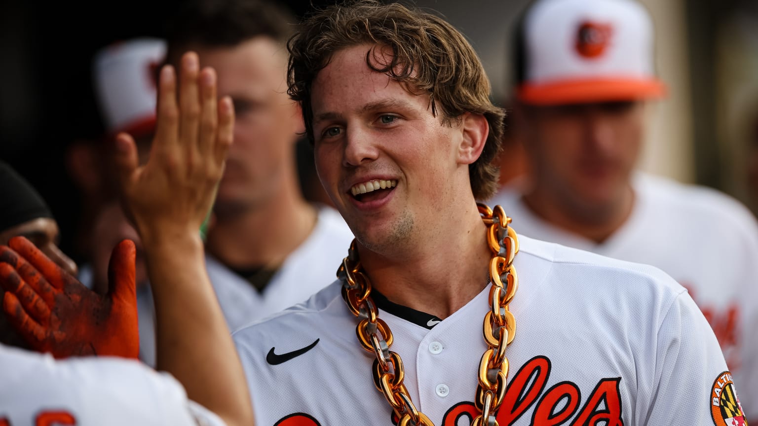 The Orioles' Adley Rutschman wears a large gold chain and high-fives a teammate in the dugout