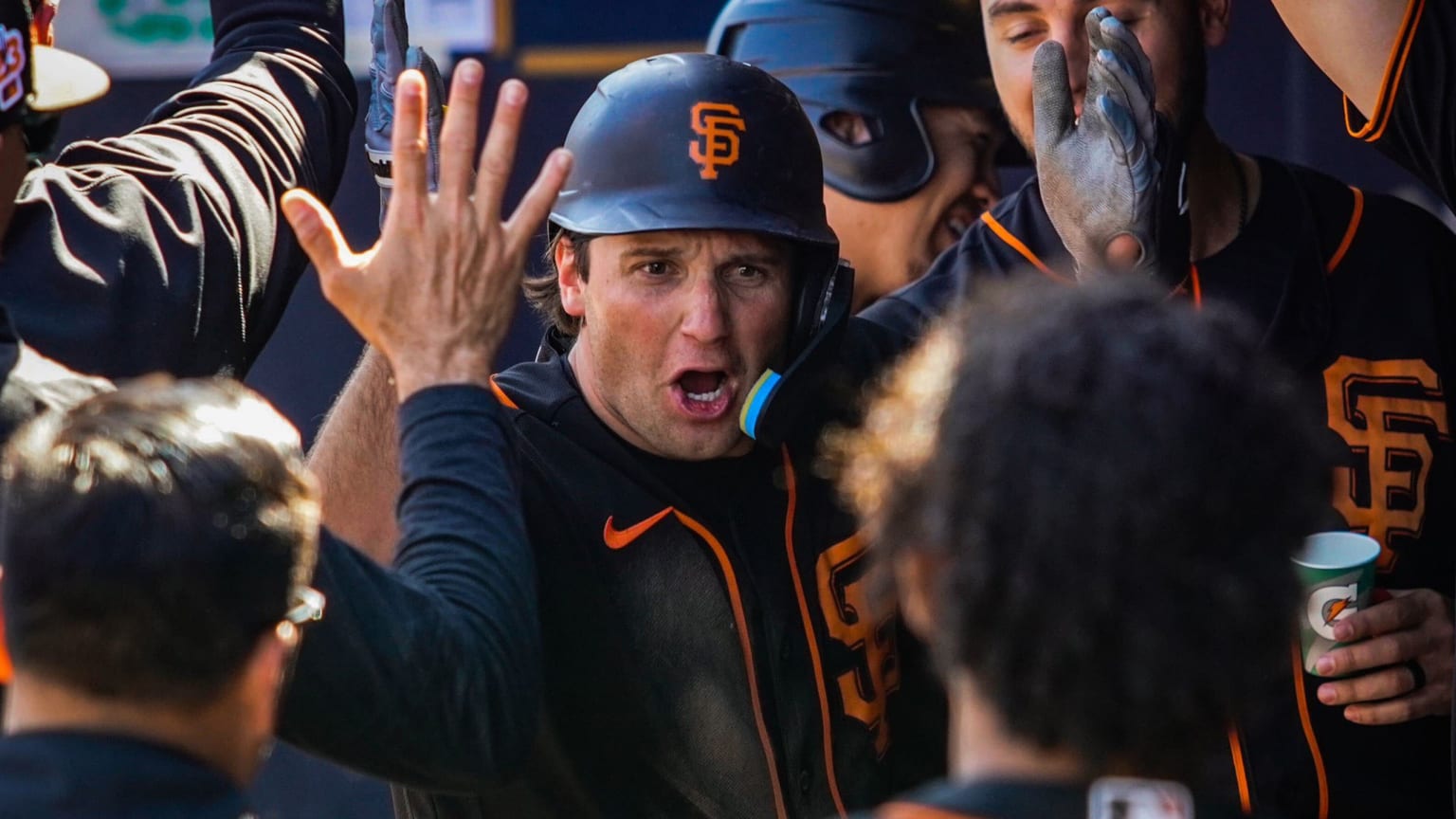 A player in a black jersey and helmet receives high-fives in the dugout