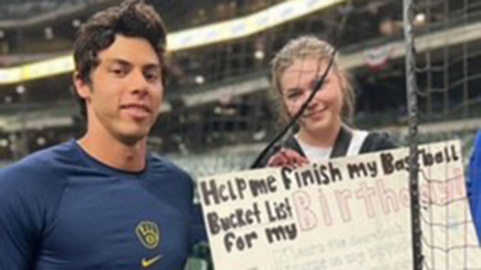 Christian Yelich stands next to a fan at the ballpark holding a sign on her birthday