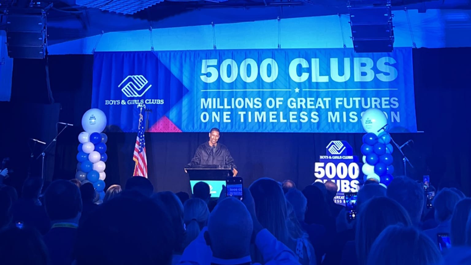 A man stands at a lectern in front of a banner with the Boys & Girls Club logo reading, ''5000 Clubs: Millions of great futures, one timeless mission''