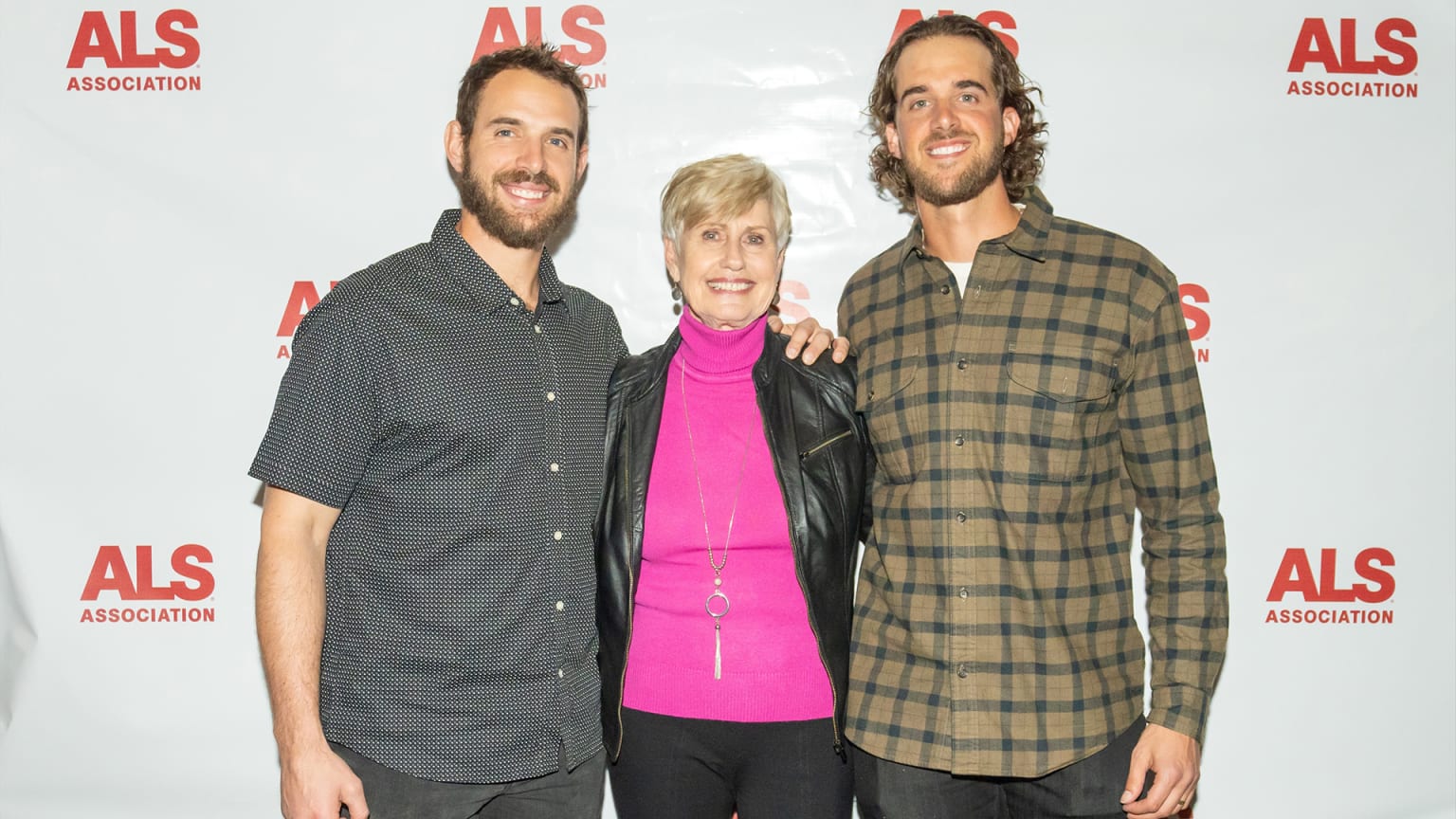 Two men stand with their arms around a shorter woman between them