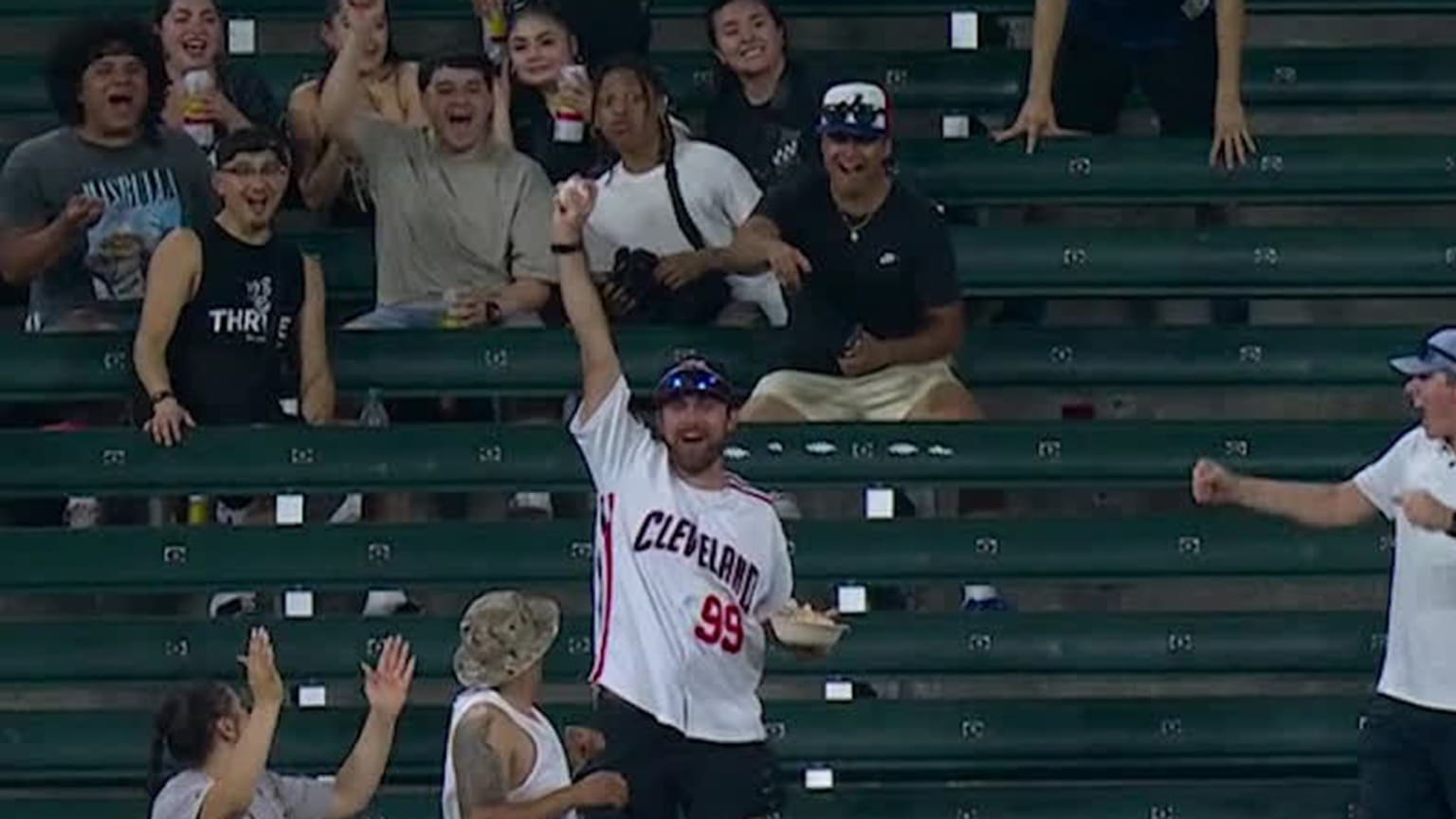 A fan holds up a baseball in his right hand while holding a bowl of food in his left