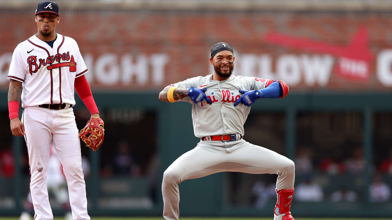 A Braves player stands to the side as a Phillies player celebrates by drawing his fingers across the team name on his jersey