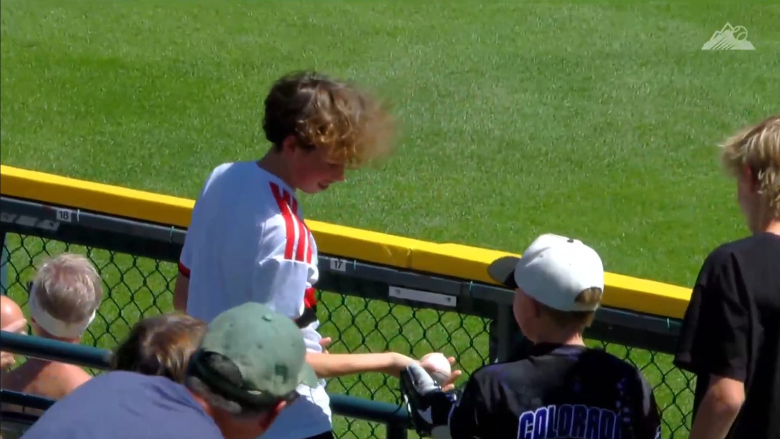 A boy at the Rockies game hands a ball to another young fan A boy at the Rockies game hands a ball to another young fan