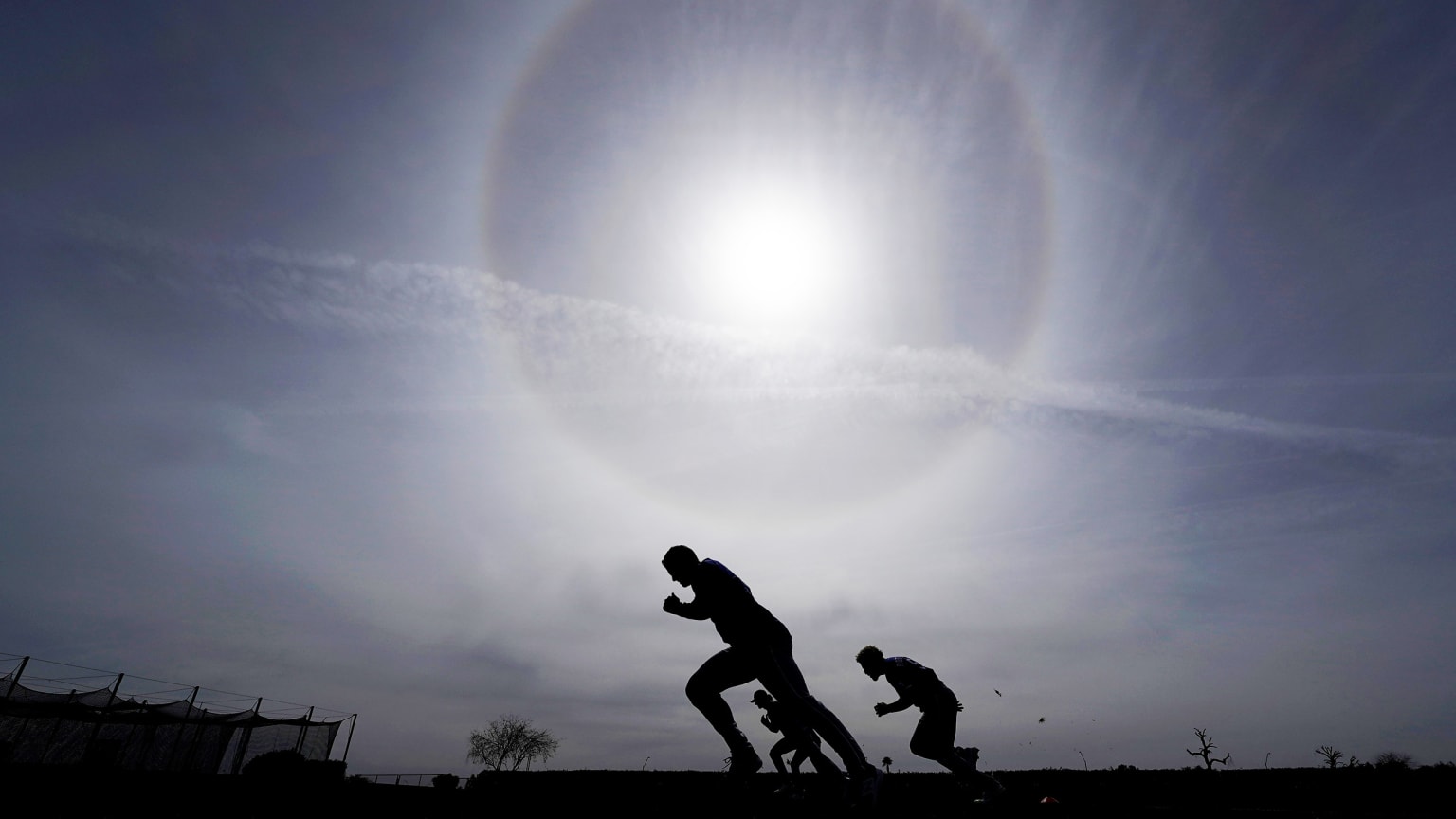 Players silhouetted against the morning sun work out on a baseball field