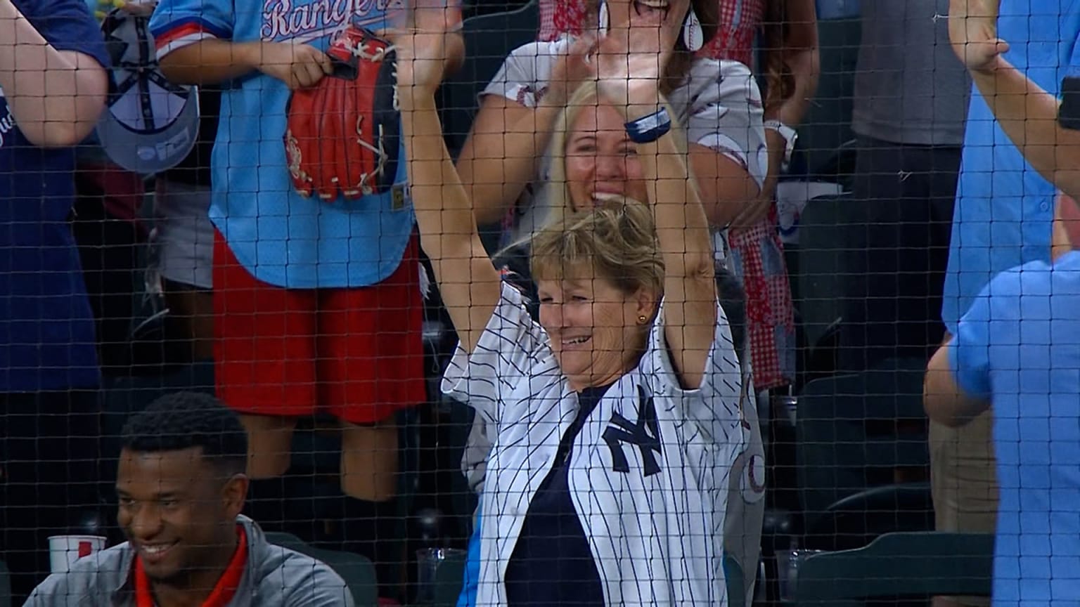 A woman in a Yankees jersey raises her hands in the air and smiles