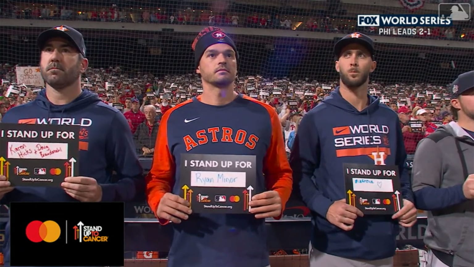 Three Astros hold up placards for Stand Up 2 Cancer