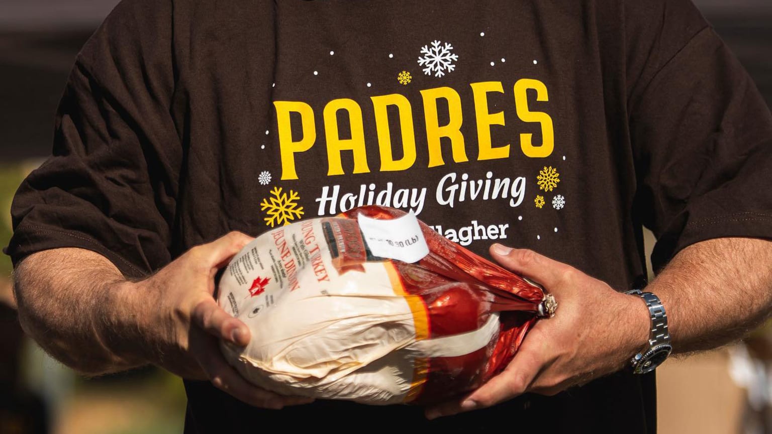 A man wearing a Padres shirt holds a Thanksgiving turkey
